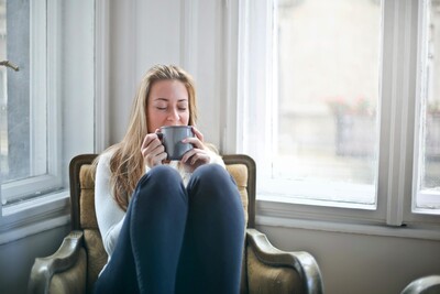 A relaxed and happy woman sitting on a chair and drinking a warm beverage